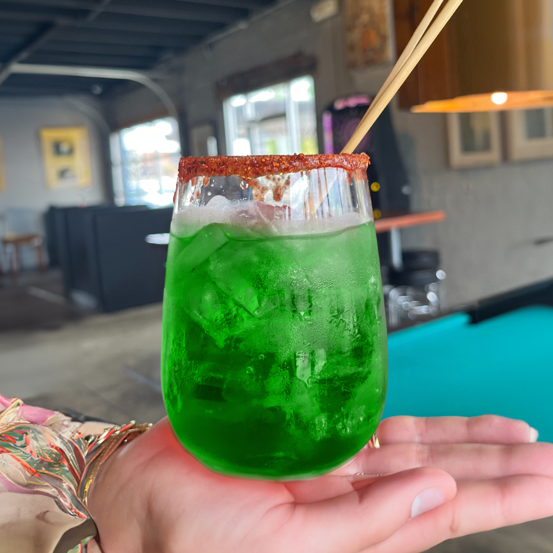 A green margarita drink on a person's hand.
