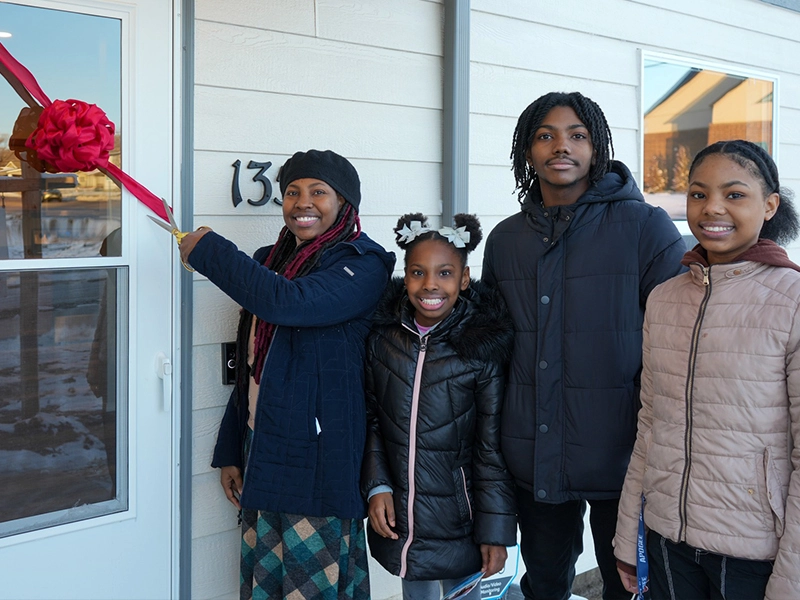 Family partner Naomi and her children cutting the ribbon at the home dedication ceremony.